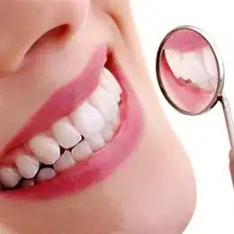 Close-up of person's smile showing white teeth with dental mirror reflection against pink background.