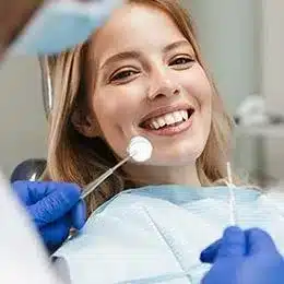 Young woman smiling during dental examination in modern dental office with dentist holding mirror.